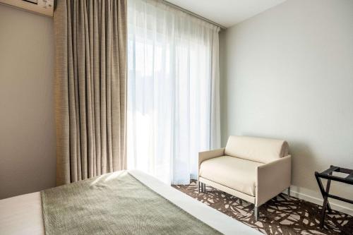 a bedroom with a bed and a chair next to a window at Quality Hotel Pau Centre Bosquet in Pau