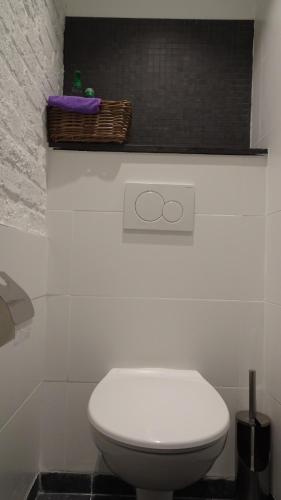a bathroom with a white toilet and a basket on the wall at La Miellerie in Huppaye