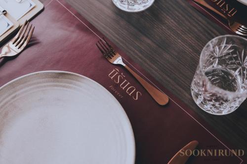 a table with a white plate and forks and glasses at SOOKNIRUND HOTEL in Chiang Rai