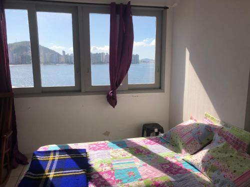 ein Schlafzimmer mit einem Bett mit Steppdecke und zwei Fenstern in der Unterkunft APARTAMENTO FRENTE A PRAIA SAO VICENTE in São Vicente