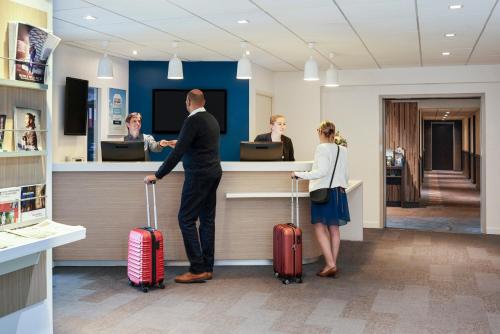 a man and a woman standing at a counter with luggage at Kyriad Le Mans Est in Le Mans