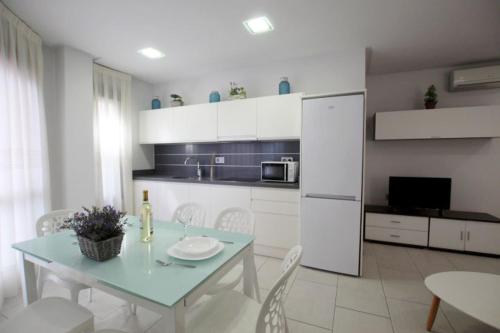 cocina blanca con mesa y nevera blanca en Apartamento Bajo 3 Dúplex Marjal playa centro de Guardamar, en Guardamar del Segura