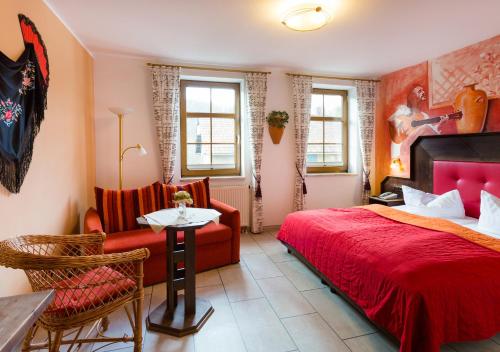 a bedroom with a red bed and a table and chairs at Hotel & Ferienwohnungen Bohlenblick in Saalfeld