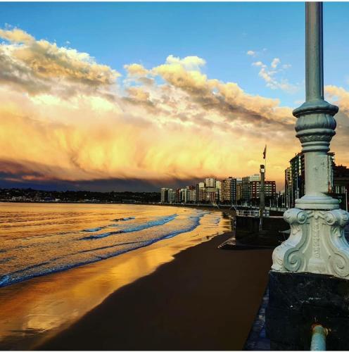 a pole on a beach with the ocean and buildings at ALBOR II in Gijón