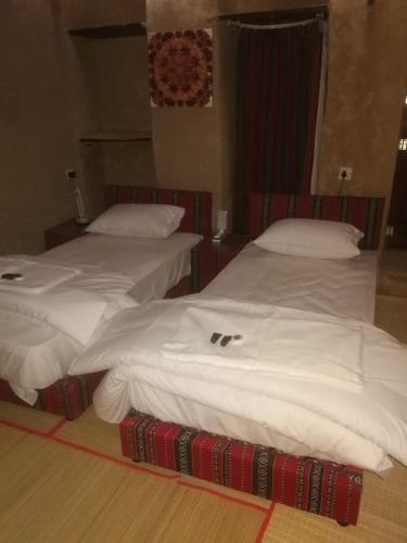 two beds in a hotel room with white sheets at Al Hamra Old House in Al Ḩamrāʼ