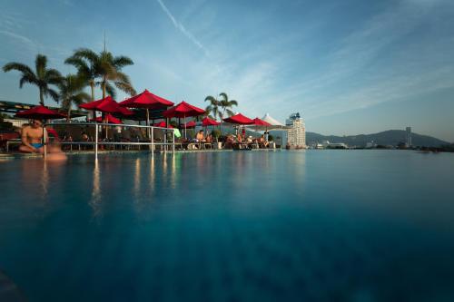 a swimming pool with red umbrellas and people sitting at The Charm Resort Phuket in Patong Beach