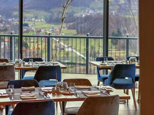 a restaurant with tables and chairs and a large window at Tarcin Forest Resort & Spa Sarajevo - MGallery Collection in Tarčin