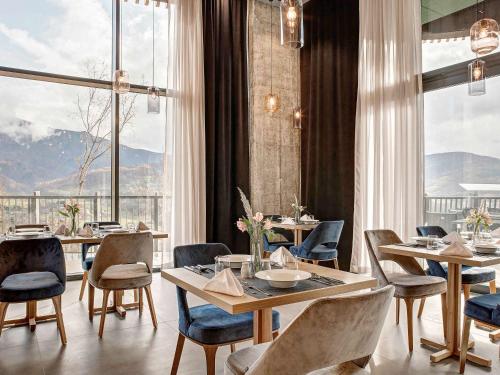 a restaurant with tables and chairs and large windows at Tarcin Forest Resort & Spa Sarajevo - MGallery Collection in Tarčin