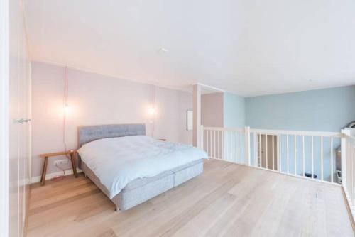 a white bedroom with a bed and a wooden floor at Hip split level apartment on the ground floor in Amsterdam