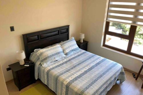 a bedroom with a bed with a striped comforter and a window at Departamento en Edificio Costanera Playa Villarrica in Villarrica
