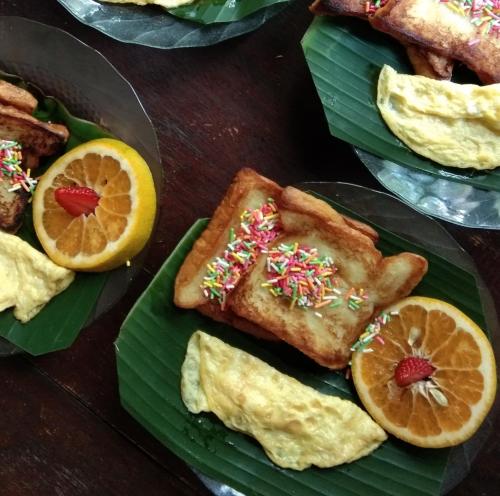 a table with a plate of food with oranges and pastries at Latansa inn in Karimunjawa
