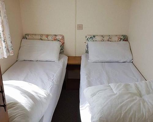 two beds in a small room with white sheets at Caravan Golden Palm in Chapel Saint Leonards