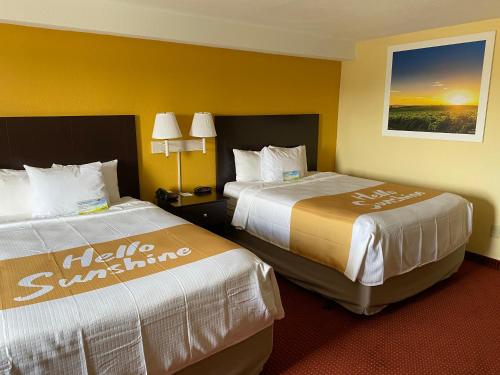2 Betten in einem Hotelzimmer mit gelben Wänden in der Unterkunft Days Inn & Suites by Wyndham Des Moines Airport in Des Moines