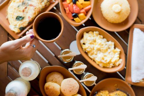 a table with plates of food and a person holding a cup of coffee at Vila Gaia Guest House in Alto Paraíso de Goiás
