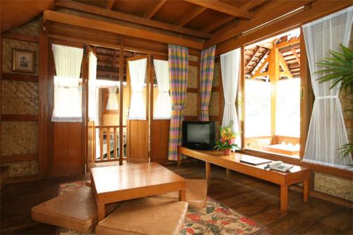 ein Wohnzimmer mit einem TV, einem Tisch und Fenstern in der Unterkunft Kampung Sumber Alam Garut in Garut