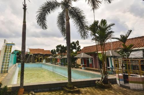 a pool with palm trees in front of a house at SPOT ON 2488 Villa Tirta Melati Syariah in Banjar