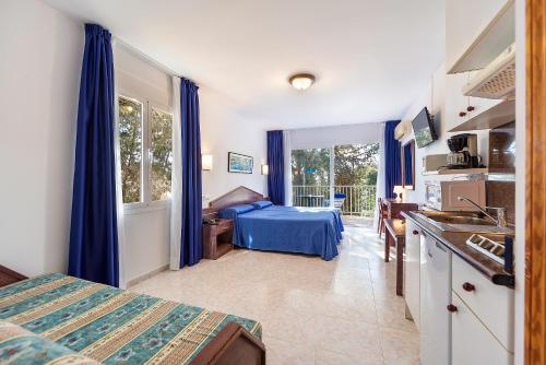 a bedroom with a bed and a kitchen with blue curtains at Apartamentos Cala Murada Minigolf in Cala Murada
