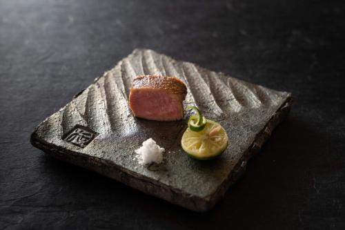 a piece of meat and a lemon on a plate at THE JUNEI HOTEL Kyoto in Kyoto