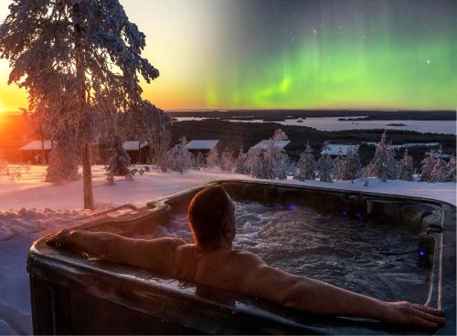 un homme assis dans un bain à remous sous l'aurore dans l'établissement Jättiläisenmaa, à Paltamo