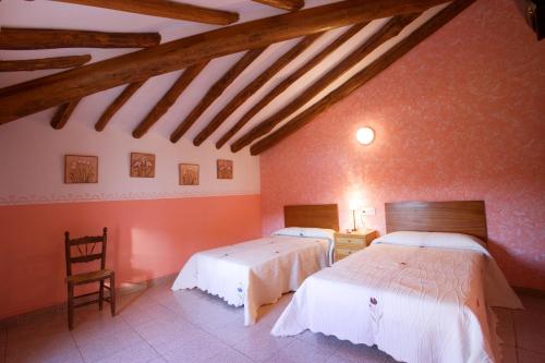 Habitación con 2 camas, paredes de color naranja y vigas de madera. en Hostal Las Rumbas, en Nuévalos