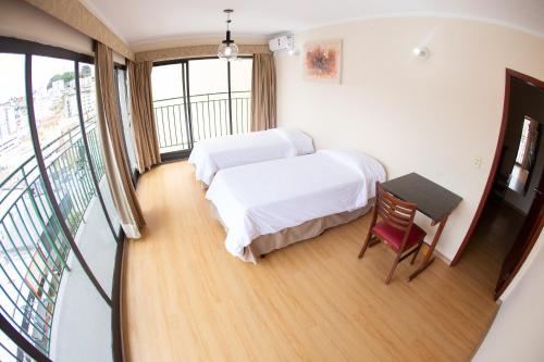a bedroom with two beds and a table and a balcony at Hotel Nacional Inn Poços de Caldas - Lazer completo e Gastronomia no Centro in Poços de Caldas