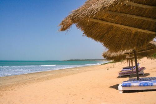 a beach with a straw umbrella and chairs and the ocean at Tamba Kuruba Eco-lodge in Folonko