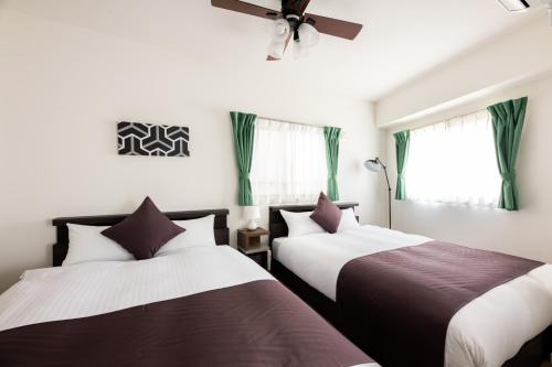 two beds in a room with windows and a ceiling fan at Grand Inn Canalside in Fukuoka