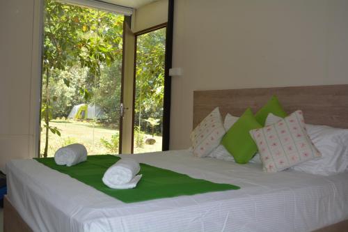 a bedroom with a bed with green and white pillows at Shadow Grove Camping & Cabins Kitulgala in Kitulgala