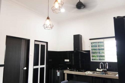 a kitchen with black cabinets and a sink and lights at Serantau Mayang by the Bliss in Bagan Serai