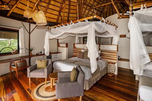 a bedroom with a canopy bed and two chairs at Lemala Wildwaters Lodge in Kangulumira