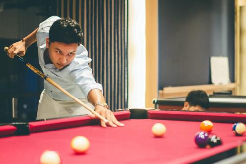 a man standing over a pool table with a cue at Divalux Resort & Spa Bangkok, Suvarnabhumi Airport-Free Shuttle in Lat Krabang