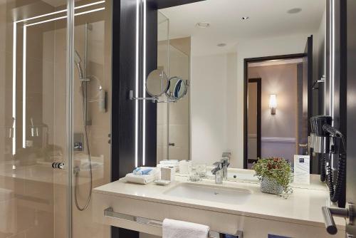a bathroom with a sink and a shower with a mirror at Dorint Hotel Frankfurt/Oberursel in Oberursel