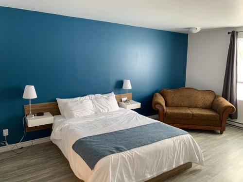 een slaapkamer met een blauwe muur en een bed en een stoel bij Motel Le Rond Point in Metabetchouan