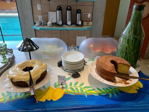 Una mesa con dos pasteles y platos encima. en Pousada Jeito de Minas, en Governador Valadares