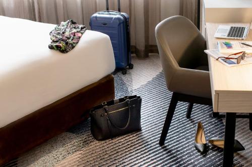 a hotel room with a bed and a chair and a suitcase at Novotel Sydney Parramatta in Sydney