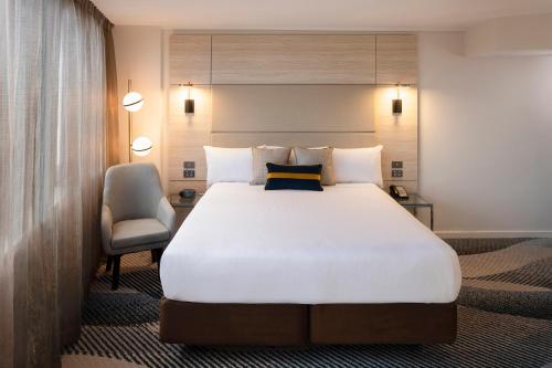 um quarto com uma grande cama branca e uma cadeira em Novotel Sydney Parramatta em Sydney