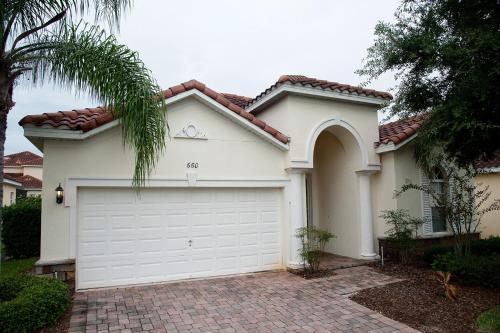 a white house with a garage and a palm tree at Four-Bedroom Pool Home Kissimmee in Orlando