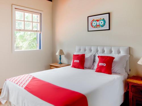 um quarto com uma cama branca e almofadas vermelhas em OYO Pousada Estrada Das Águas, São João del Rei em São João del Rei