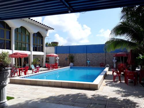 a swimming pool with red chairs and a building at Pousada Das Palmeiras in Jaboatão dos Guararapes