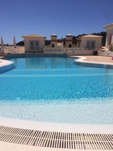 a large blue swimming pool with buildings in the background at Modern Two Bedroom Poolside Townhouse in Budens