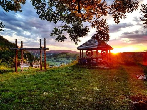 a gazebo and a swing in a field with the sunset at Log cabin Uvac (Vikendica Saponjic) in Nova Varoš