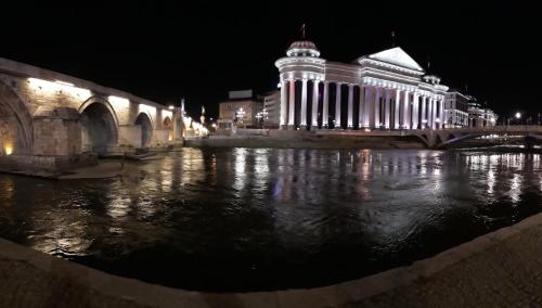 a lit up building next to a river at night at Hotel Square in Skopje