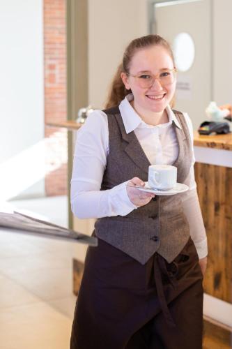 a woman holding a cup of coffee on a plate at Hotel Achterum Greetsiel in Greetsiel