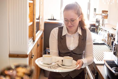 a woman holding a tray with a cup of coffee at Hotel Achterum Greetsiel in Greetsiel