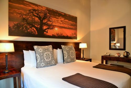 a bedroom with a large white bed with a painting on the wall at Bushveld Terrace Safari Hotel, Lodge & Spa in Phalaborwa