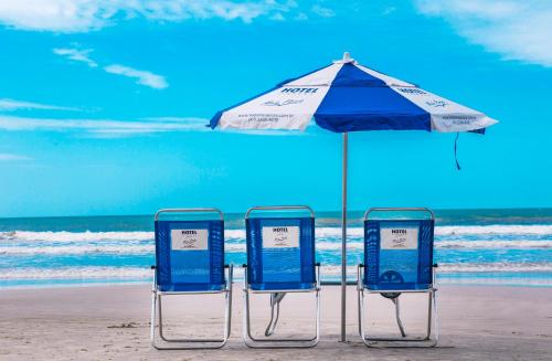 três cadeiras debaixo de um guarda-sol na praia em Hotel Itapema Meia Praia em Itapema