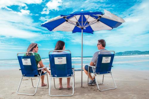two people sitting in chairs under an umbrella on the beach at Hotel Itapema Meia Praia in Itapema