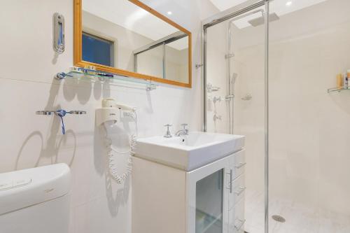 La salle de bains blanche est pourvue d'un lavabo et d'une douche. dans l'établissement Anchors Aweigh - Adult & Guests Only, à Narooma