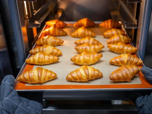 a person holding a tray of croissants in an oven at Super Hotel Okayama Station Higashiguchi in Okayama