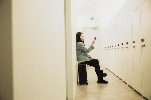 a woman sitting in a locker room taking a picture at Capsule Hotel City Cabin Susukino in Sapporo